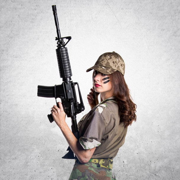 Militaire vrouw met een geweer op gestructureerde grijze achtergrond - Foto, afbeelding