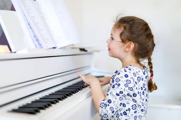 Beautiful little kid girl playing piano in living room or music school - Foto, afbeelding