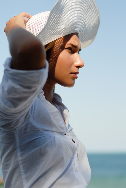 Young woman resting by the sea and wearing white hat - Фото, зображення