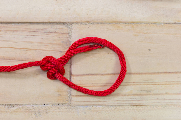 Bowline-Knoten aus rotem synthetischem Seil, Festziehen auf Holzgrund. - Foto, Bild