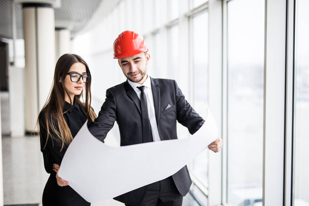 businessman architects look at paper plan business woman architect in office to discuss business projects. Successful young engineer in construction helmet with young woman are on table - Photo, Image