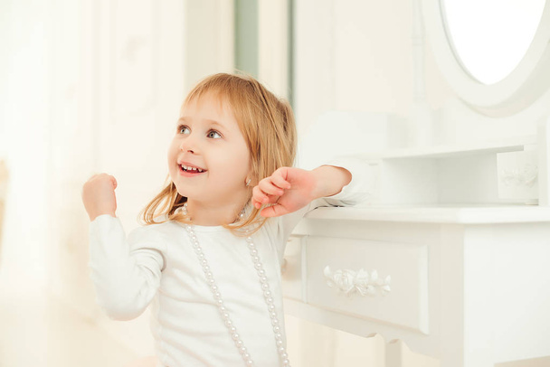 Portret van een schattig klein meisje zit in de buurt van een spiegel op de lichte kamer. - Foto, afbeelding