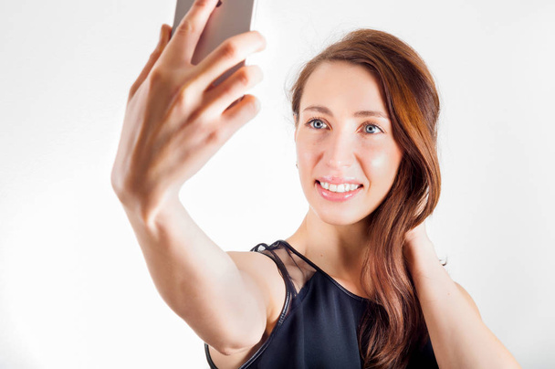 Nuori nainen käyttää älypuhelinta ampua selfie ja hymyilevä
. - Valokuva, kuva