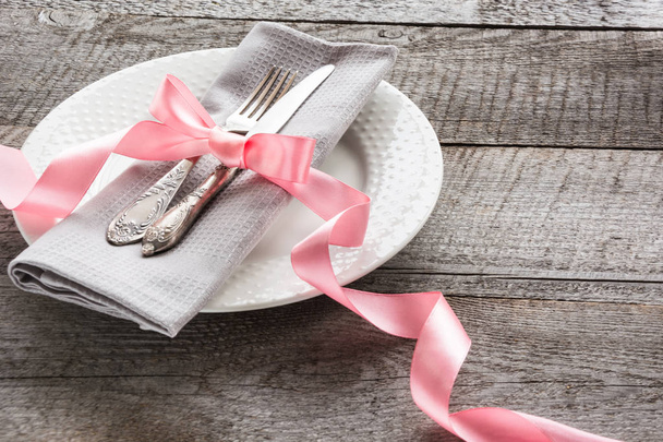 Elegance table setting with pink ribbon on wooden board. Rustic stile. Romantic dinner. Top view. - Foto, afbeelding