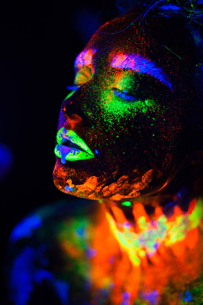 Beautiful extraterrestrial model woman in neon light. It is portrait of beautiful model with fluorescent make-up, Art design of female posing in UV with colorful make up. Isolated on black background - Photo, image