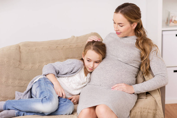 happy pregnant woman and girl on sofa at home - Foto, immagini