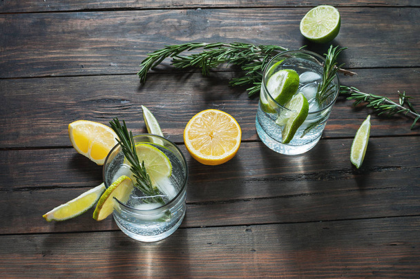 Alcoholic drink with lemon, rosemary and ice on rustic wooden table - Foto, Bild