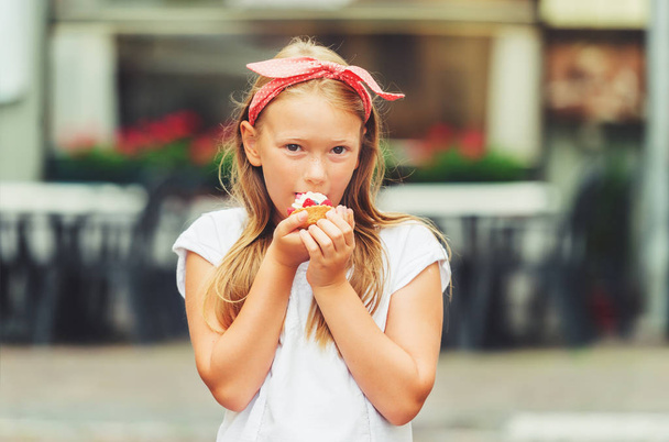 Grappige meisje eten taart buitenshuis, het dragen van rode polka dot hoofdband - Foto, afbeelding