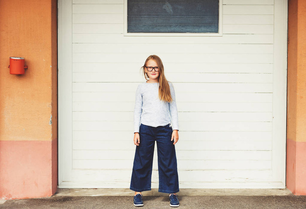 Venkovní legrační portrét roztomilý malý 9-10 let stará dívka, která nosí modré nahoře, Jeans kalhotové sukně a brýle  - Fotografie, Obrázek