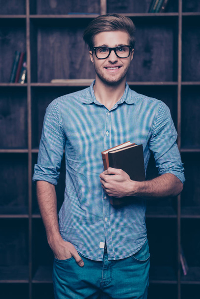 An attractive young guy in glasses standing in front of shelves, - Fotó, kép