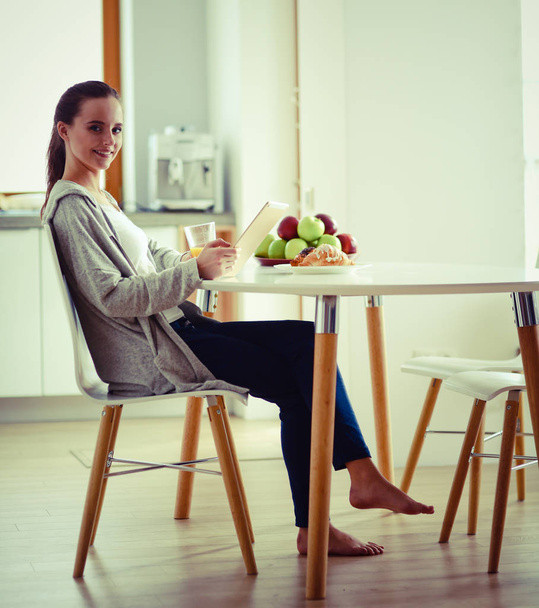 Young woman with orange juice and tablet in kitchen - Photo, image