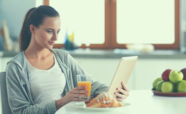 Young woman with orange juice and tablet in kitchen - Foto, imagen