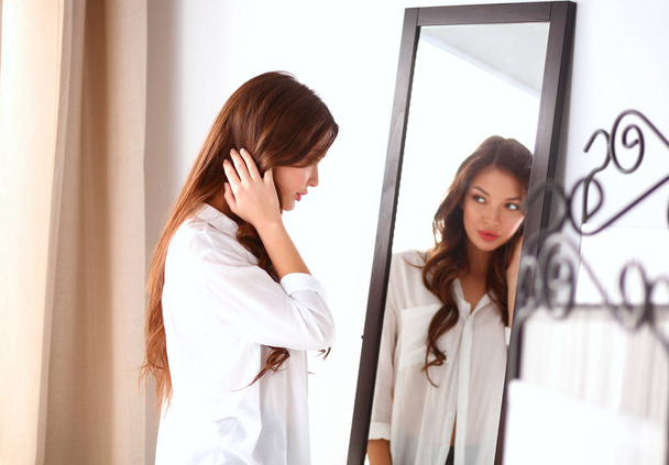 Young woman looking herself reflection in mirror at home - Foto, imagen