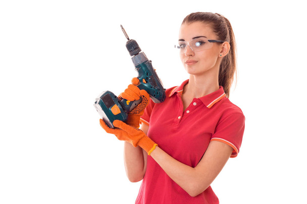 beautiful young girl in a red t-shirt and goggles holds drill - Foto, imagen