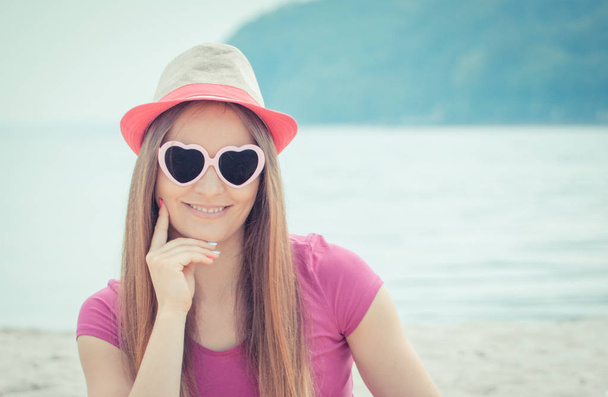 Mulher feliz turista em chapéu de palha e óculos de sol sentado na praia, tempo livre à beira-mar
 - Foto, Imagem