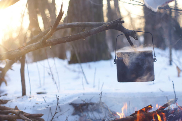 Ein Topf mit kochendem Wasser auf dem Feuer wärmt im Winterwald, - Foto, Bild