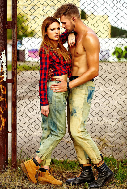 Sexy stylish blond young woman model with bright makeup with perfect sunbathed skin and handsome muscled man in jeans outdoors - Foto, Bild