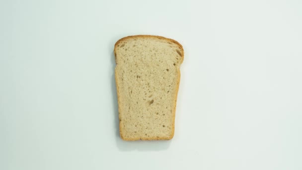 A slice of bread over white background. Bite off pieces of the bread slice. Top view. Stop motion - Materiał filmowy, wideo