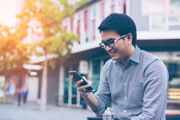 Jonge Aziatische knappe zakenman lacht tijdens het lezen van zijn smart - Foto, afbeelding