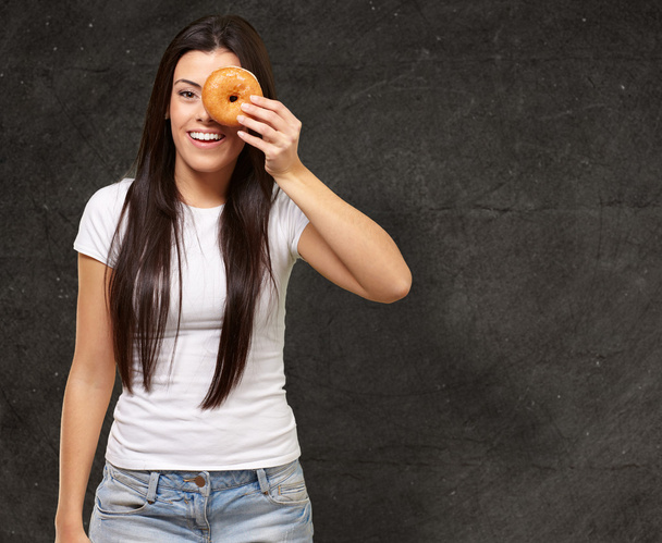 Portret van een jonge vrouw op zoek via een donut tegen een grunge - Foto, afbeelding