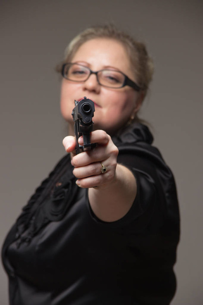 Adult business woman with black gun on a gray background - Foto, Imagem