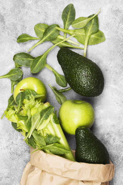 Різні зелені овочі та фрукти - селера, яблука, авокадо, шпинат у паперовій упаковці на світлому фоні. Вид зверху. Фундамент їжі
 - Фото, зображення