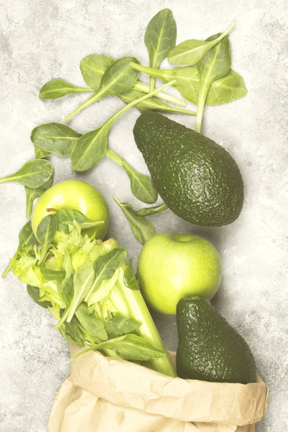 Various green vegetables and fruit - celery, apples, avocado, spinach in a paper package on a light background. Top view. Food background. Toning - Foto, afbeelding