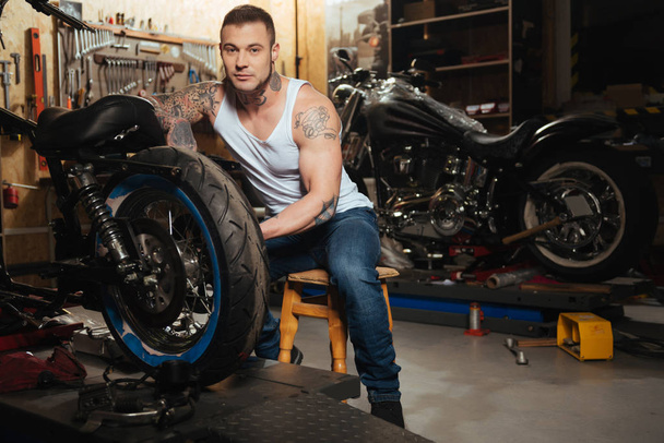 Handsome motorcyclist posing in the workshop - Photo, Image