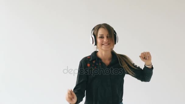 Slow motion of young woman in headphones listening music and dancing on white background indoors - Video, Çekim