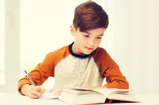 student jongen met boek schrijven naar notebook thuis - Foto, afbeelding