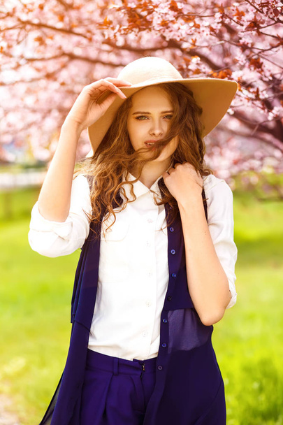 Outdoor portrait of young beautiful fashionable lady posing near flowering tree. Model wearing stylish accessories & clothes. . Female beauty & fashion. City lifestyle.  - Foto, afbeelding