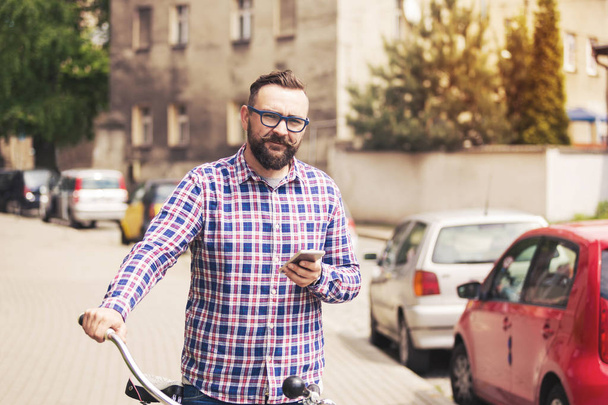 Young trendy man holding bike handlebar and mobile - Фото, изображение