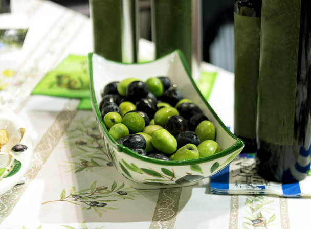 зелені та чорні оливки в порцеляновій тарілці на столі
 - Фото, зображення