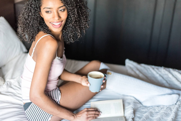 vrouw lezen van een boek en koffie drinken op bed met sokken - Foto, afbeelding