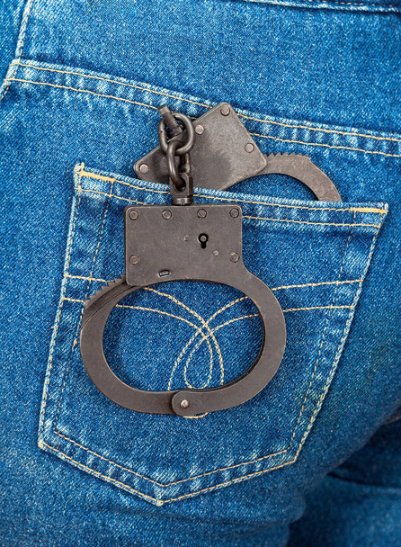 Черные металлические наручники в заднем кармане джинсов
 - Фото, изображение