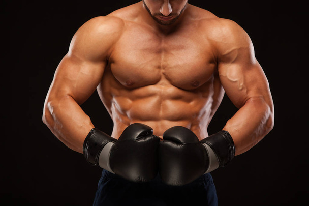 Muscular young man with perfect Torso with six pack abs, in boxing gloves is showing the different movements and strikes isolated on black background with copyspace - Фото, зображення