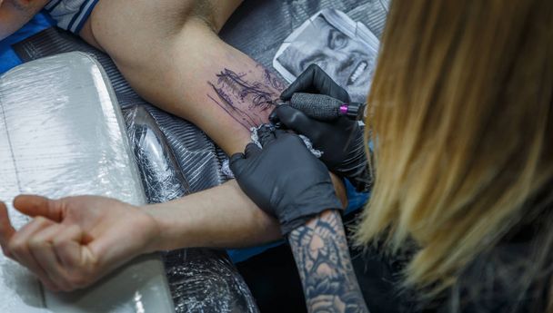 Une fille blonde tatoueuse représente un tatouage sur le bras d'un cl
 - Photo, image