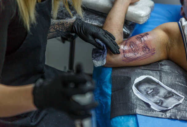 ein tätowiertes Mädchen zeichnet ein Tattoo auf den Arm eines Jungen - Foto, Bild