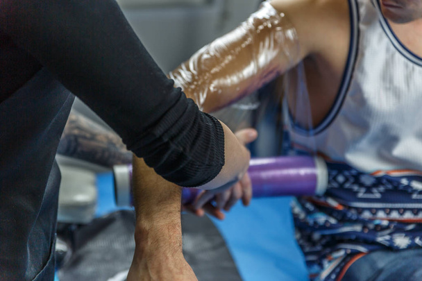 A tattoo artist is covering a tattoo on the arm of a boy - Φωτογραφία, εικόνα