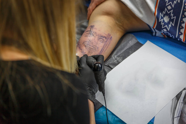 Una ragazza tatuatrice ritrae un tatuaggio sul braccio di un ragazzo
 - Foto, immagini