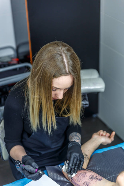 Ένα κορίτσι τατουάζ καλλιτέχνης απεικονίζει ένα τατουάζ με το τατουάζ μηχάνημα - Φωτογραφία, εικόνα