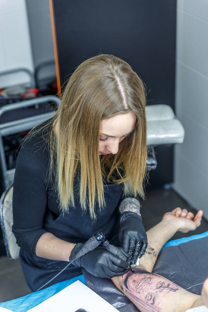Μια γυναίκα καλλιτέχνης τατουάζ χρωματίζει ένα τατουάζ με το τατουάζ μηχάνημα - Φωτογραφία, εικόνα