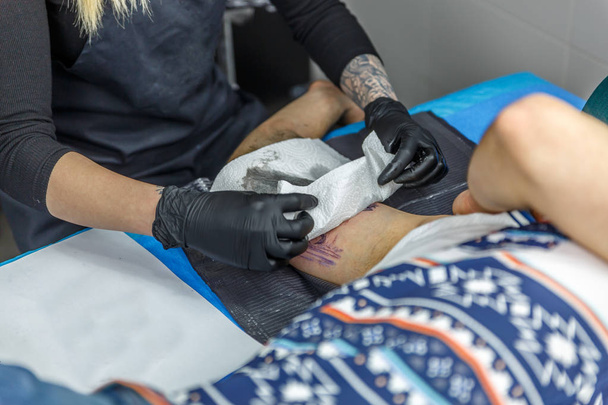 Μια γυναίκα καλλιτέχνη τατουάζ είναι ζωγραφική ένα τατουάζ με το τατουάζ μηχάνημα - Φωτογραφία, εικόνα