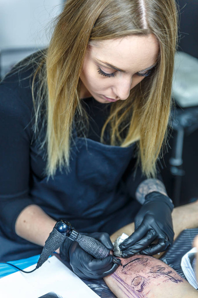 Artista loira bonita está fazendo uma tatuagem com concentração máxima
 - Foto, Imagem