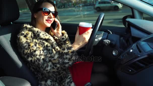 Mulher bonita em um casaco de pele usando um smartphone e beber café no carro
 - Filmagem, Vídeo
