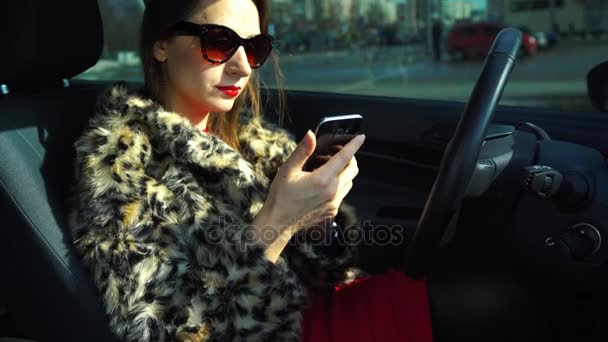 Mooie vrouw in een bontjas met behulp van een smartphone en drinken koffie in de auto - Video