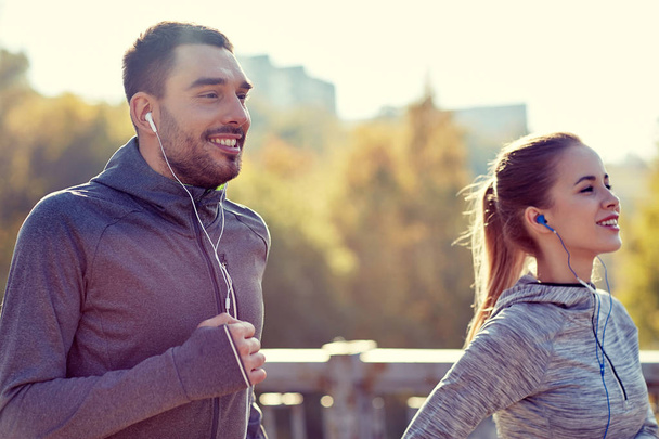 happy couple with earphones running in city - 写真・画像