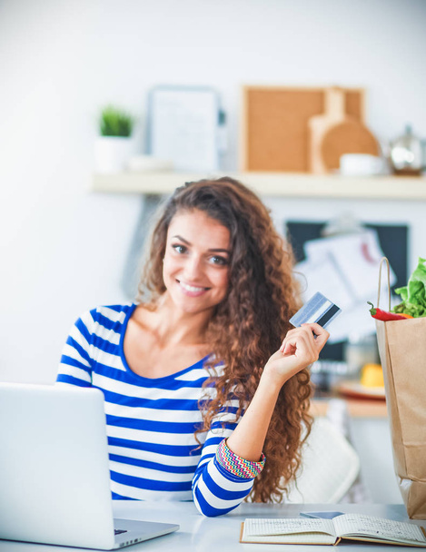 Smiling woman online shopping using computer and credit card in kitchen - Fotografie, Obrázek