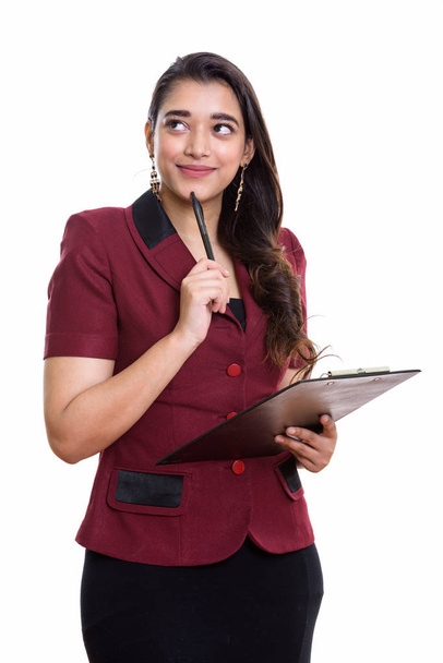 Young beautiful Indian businesswoman holding clipboard while thinking and looking up - Foto, Imagen