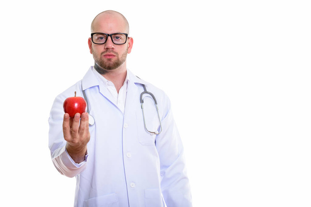 Estudio de tiro de joven calvo musculoso médico hombre sosteniendo manzana roja - Foto, imagen